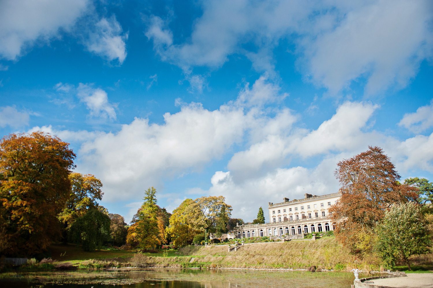 Beautiful overview of Cowley Manor of the lake, Autumnal tree's and blue sky.