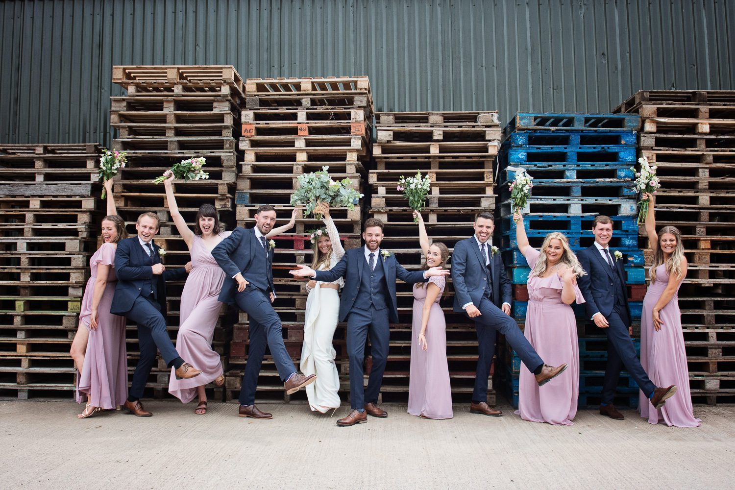 Bridal party striking poses next to wooden pallets. Looks fun. In Gloucester