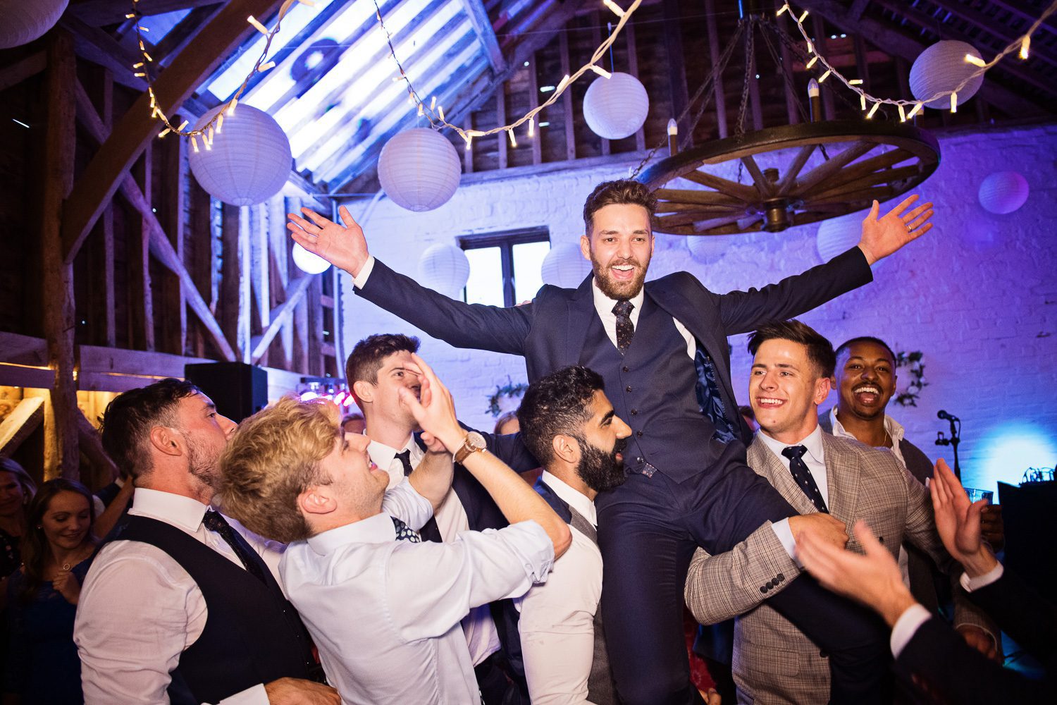A groom being picked up in the air by his friends during his wedding party.