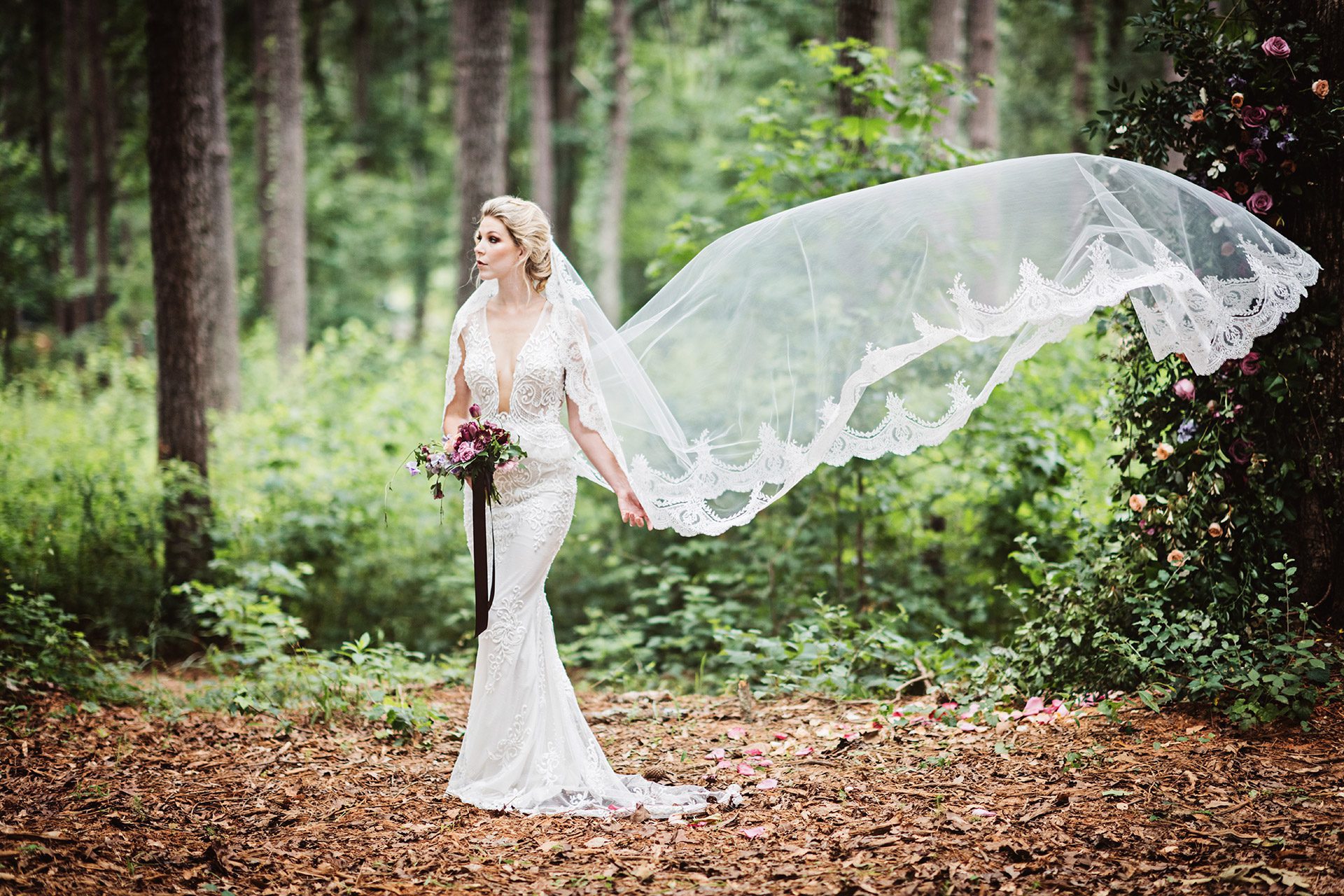 A bride stood on her own in a forest with a magnificent veil floating in the air.