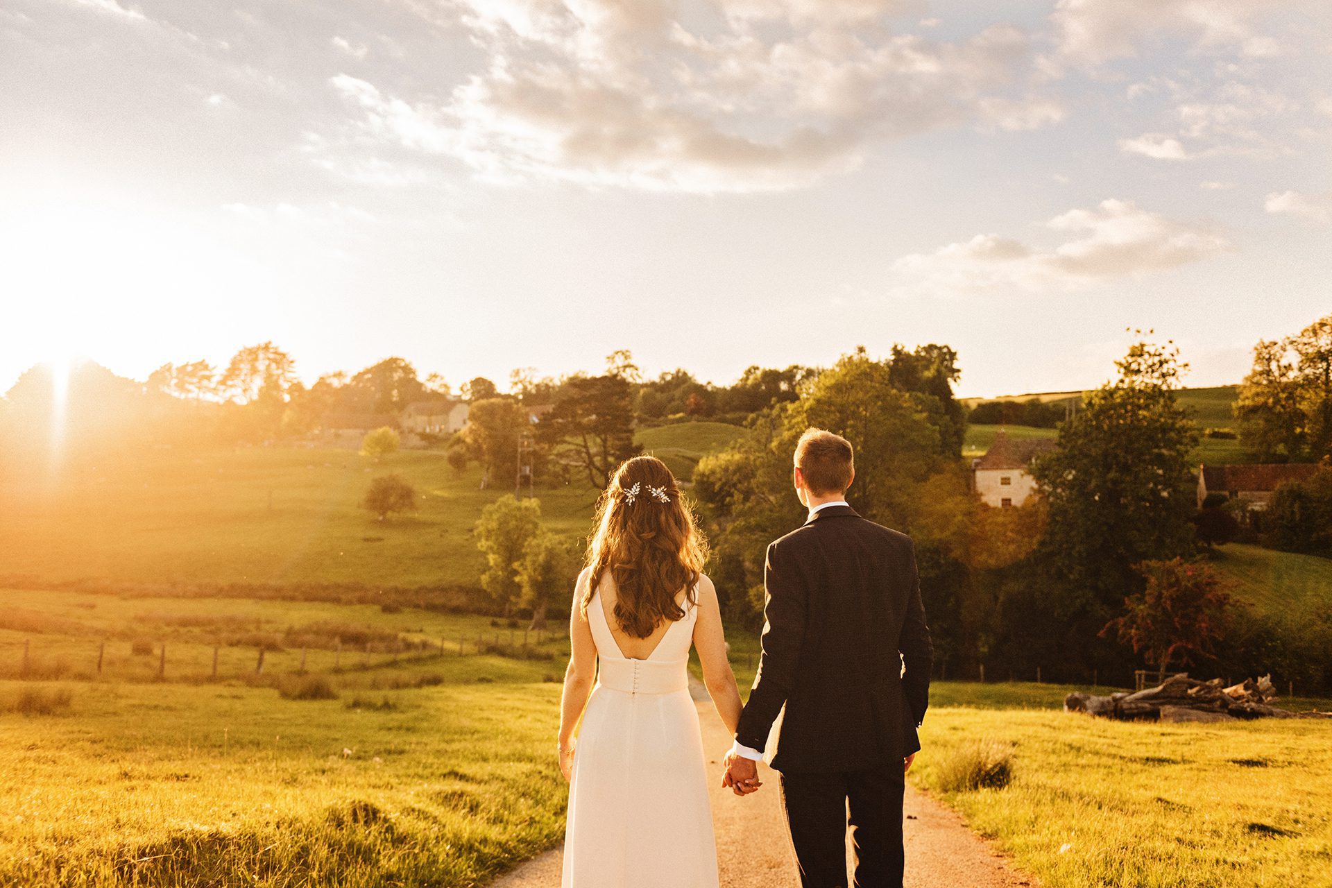Bride and groom holding hands during a brilliant sunset over their wedding venue, The Kingscote Barn